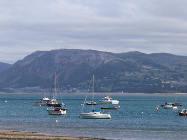 Several sailboats and motorboats anchored in a bay with a mountainous landscape in the background at Gadlys House - Waters Edge in Beaumaris