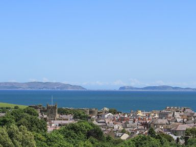A coastal town with rooftops trees and a church tower by the sea with hills in the background at Gadlys House Waters Edge Beaumaris