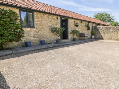 An exterior view of a stone building with a tiled roof and a small concrete patio with potted plants and a bench at Puddleducks Sherborne