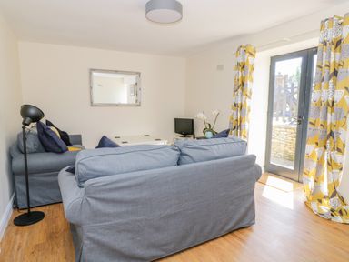 A living room with two grey sofas a floor lamp a small TV on a table and yellow patterned curtains at Puddleducks in Sherborne