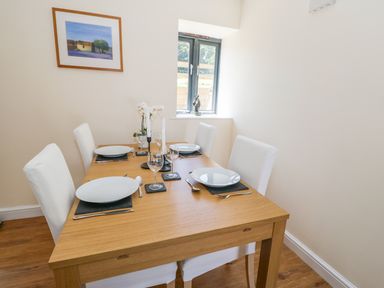 A dining room with a wooden table set for four with white plates and chairs at Puddleducks in Sherborne