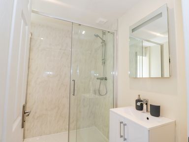 A bathroom with a glass shower enclosure a wall-mounted shower head and a white vanity with a mirror above it at Puddleducks in Sherborne