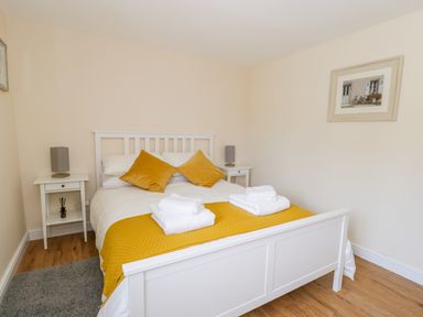 A bedroom with a white bed frame yellow cushions and a yellow bed runner at Puddleducks in Sherborne