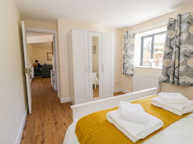 A bedroom with a bed folded towels a white wardrobe and patterned curtains at Puddleducks in Sherborne