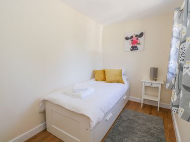 A small bedroom with a single white bed with yellow pillows a bedside table with a lamp and a curtain at Puddleducks in Sherborne
