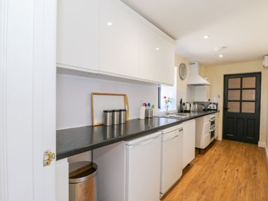 A kitchen with white cabinets black countertop appliances and wooden floor at Puddleducks in Sherborne