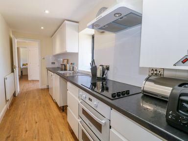 A narrow kitchen with white cabinets black countertops a stove toaster and kettle at Puddleducks in Sherborne