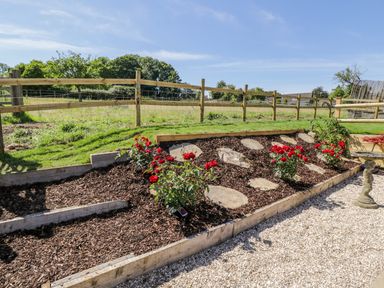 A flower bed with red flowers and stone pavers next to a wooden fence and gravel path at Puddleducks in Sherborne