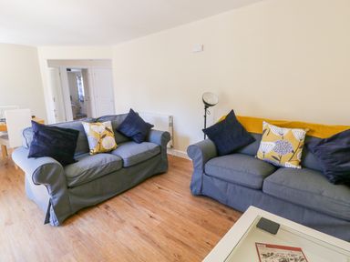 A living room with two grey sofas and cushions with a floor lamp and wooden flooring at Puddleducks in Sherborne