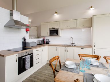 A kitchen with appliances and a dining table at Cowslip in Bamburgh