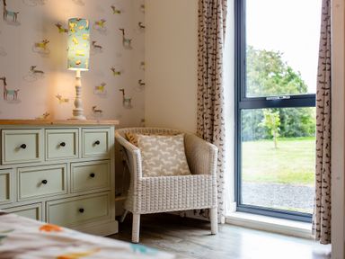 A bedroom with a lamp, dresser, and chair at Cowslip in Bamburgh