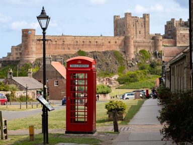 A red telephone box and street lamp with a castle in the background at Cowslip in Bamburgh