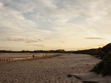 A beach with people walking along the shore at Cowslip in Bamburgh
