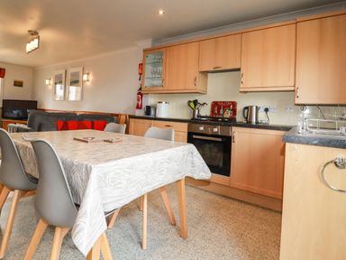 A kitchen with wooden cabinets and a dining table with chairs at Sunflower Cottage in St Issey