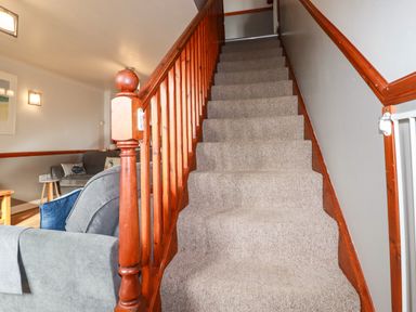 Carpeted staircase with wooden railing and gray sofas in a living area at Sunflower Cottage in St Issey