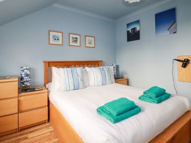 A bedroom with a wooden bed frame blue striped pillows folded teal towels on bed wooden dressers and blue wall art at Sunflower Cottage in St Issey