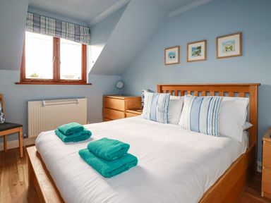A bedroom with a wooden bed with white and blue striped pillows and folded teal towels on the bed at Sunflower Cottage in St Issey