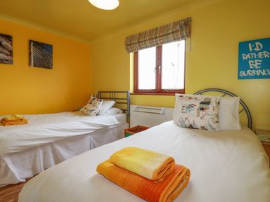 A bedroom with two single beds with folded towels on them a window and wall art at Sunflower Cottage in St Issey