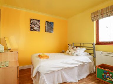 A bedroom with a single bed white linens a small wooden dresser and a window at Sunflower Cottage in St Issey