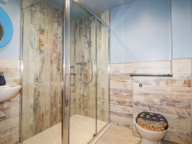A bathroom with a glass shower enclosure a toilet with a fish-themed seat and a small sink at Sunflower Cottage in St Issey