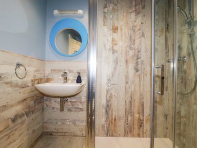 A bathroom with a wall-mounted sink a round mirror and a glass shower enclosure at Sunflower Cottage in St Issey