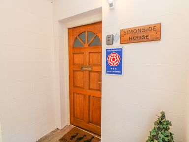 A wooden entrance door with a mail slot and a doormat a sign reading Simonside House and a self catering plaque on the wall at Simonside Apartment in Rothbury