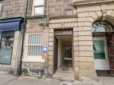 A narrow entrance passage between stone buildings with a window and an open door at Simonside Apartment in Rothbury