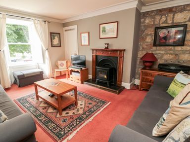 A living room with sofas a wooden coffee table a fireplace and a window at Simonside Apartment in Rothbury