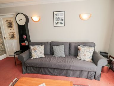 A living room with a gray sofa cushions a large clock bookshelf and two wall lights at Simonside Apartment in Rothbury
