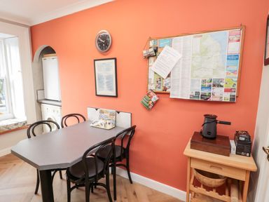 A dining area with a table and four chairs a wall clock a bulletin board and a small wooden side table at Simonside Apartment in Rothbury