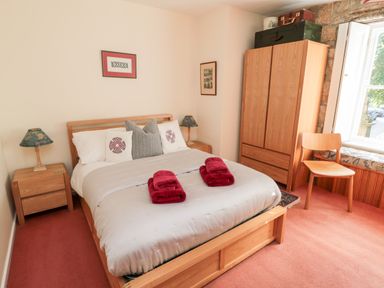 A bedroom with a bed with pillows and folded towels bedside tables with lamps a wooden wardrobe and a chair by the window at Simonside Apartment in Rothbury