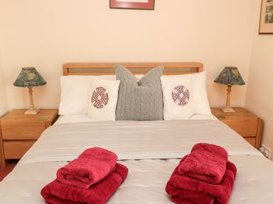 A bed with white and gray pillows red towels on the bed and wooden nightstands with lamps on each side in Simonside Apartment Rothbury
