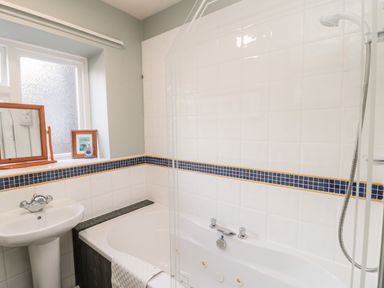 A bathroom with a bathtub shower and sink with a small mirror and framed picture on the window sill at Simonside Apartment in Rothbury