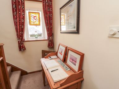 A small landing area with a window covered by red curtains a wooden desk with framed photos a notebook a pen and a no smoking sign at Simonside Apartment in Rothbury