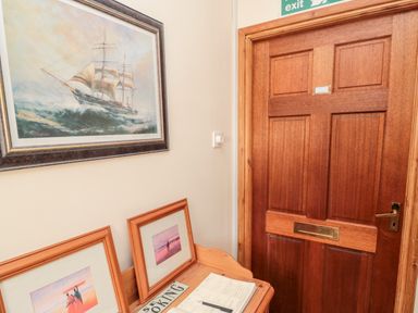 A wooden door next to a wooden bench with framed pictures and a book with a pen on it at Simonside Apartment in Rothbury