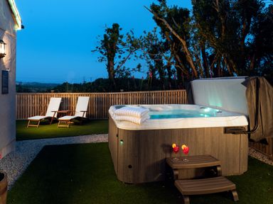 An outdoor area with a hot tub two lounge chairs and two drinks on a small table at Bear Cottage in Chacewater near Truro