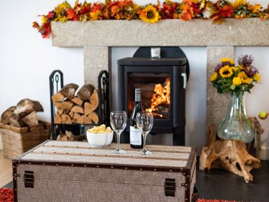 A fireplace with firewood and a wine bottle with two glasses on a table at Bear Cottage in Chacewater near Truro