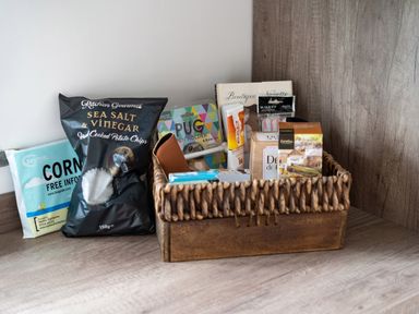 A wooden basket with assorted food and personal care items on a wooden countertop at Bear Cottage in Chacewater near Truro