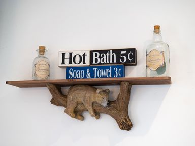 A wooden wall shelf with a carved bear figurine holding two glass bottles and vintage style signs at Bear Cottage in Chacewater near Truro