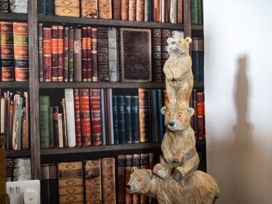 A wooden sculpture of three stacked bears in front of a bookcase filled with books at Bear Cottage in Chacewater near Truro
