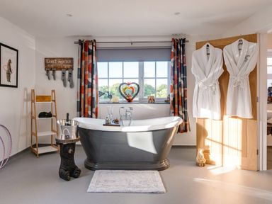 A bathroom with a freestanding bathtub and robes hanging on a door at Bear Cottage in Chacewater near Truro
