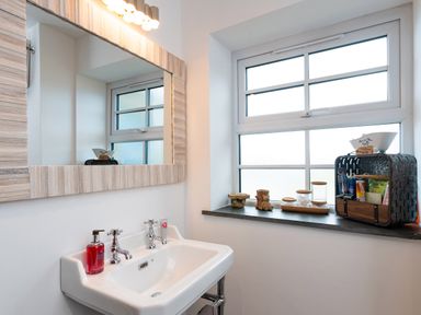 A bathroom with a white sink and mirror next to a window with toiletries on the windowsill at Bear Cottage in Chacewater near Truro