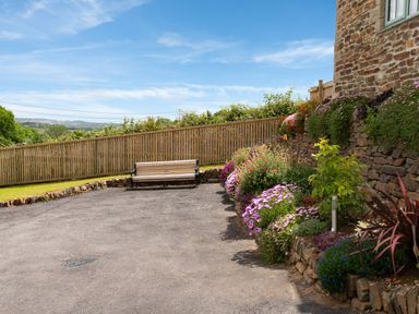 A garden area with a wooden bench stone walls and flower beds at Bear Cottage in Chacewater near Truro