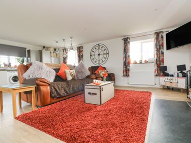 A living room with a red rug brown sofas a wall clock and a TV at Bear Cottage in Chacewater near Truro