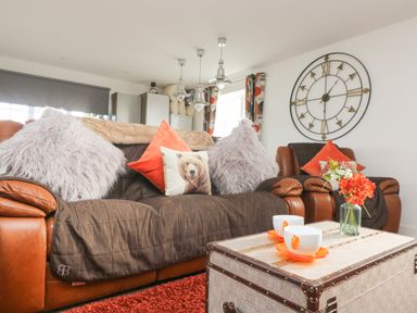 A living room with brown leather sofas pillows a large wall clock and a coffee table with cups and flowers at Bear Cottage in Chacewater near Truro