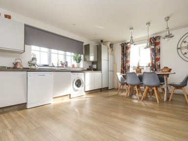 A kitchen with white cabinets a washing machine dishwasher dining table and chairs at Bear Cottage in Chacewater near Truro