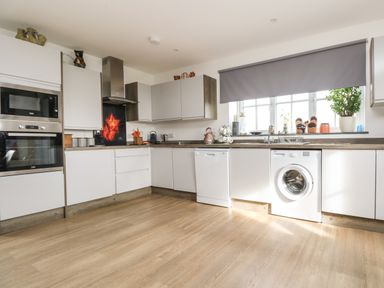 A kitchen with white cabinets wooden floor dishwasher washing machine and a window with a gray blind Bear Cottage Chacewater near Truro