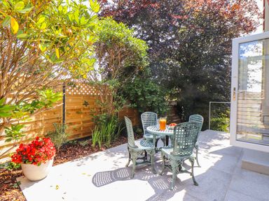 A patio with a metal table and four chairs next to plants and a wooden fence at The Crest in Helston