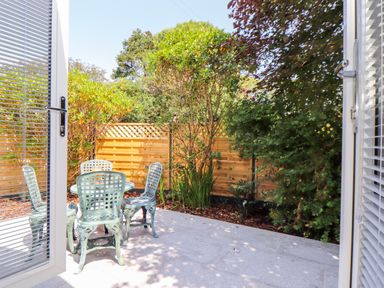 An outdoor patio with a round table and four chairs surrounded by trees and plants at The Crest in Helston