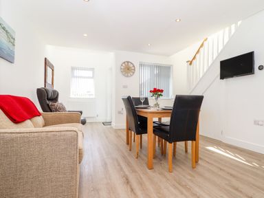 A dining area with a wooden table and black chairs next to a sitting area with a beige sofa and armchair at The Crest in Helston